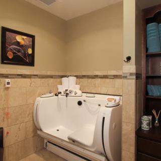A well-appointed bathroom features a unique bathtub against a tiled wall, artwork, and neatly arranged shelves with towels.