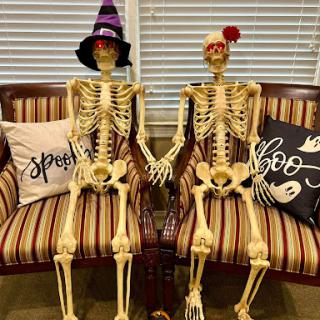 A spooky yet cute Halloween decoration featuring two skeletons holding hands, dressed in festive hats.