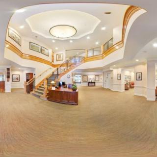 A spacious hotel lobby featuring a grand staircase and a reception desk, elegantly illuminated with modern lighting.