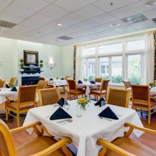 A well-lit dining room with neatly arranged tables and chairs, featuring black napkins on white tablecloths.