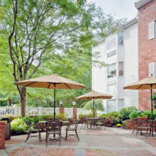 A serene outdoor patio area with tables and umbrellas, surrounded by greenery and buildings.