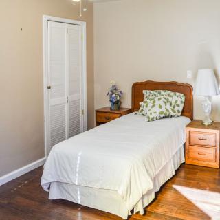 A simple bedroom with a single bed, wooden nightstands, and a lamp on a wooden floor.