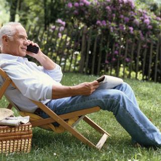 An elderly man enjoying a peaceful moment outdoors, talking on the phone while lounging in a chair.