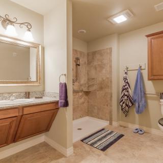 A modern bathroom with a large mirror, wooden cabinets, and a spacious tiled shower area.