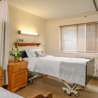 A clean and well-lit hospital room with a medical bed, nightstand, and window blinds.