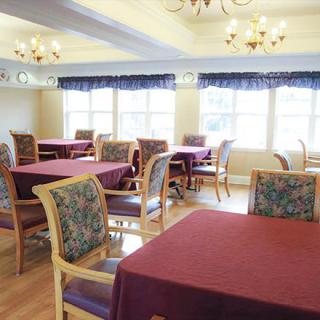 A well-lit dining room with several tables and chairs, featuring chandeliers and large windows with curtains.