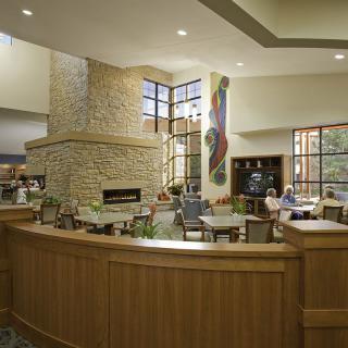 A modern lobby with a central fireplace, comfortable seating, large windows, and wood panel accents.