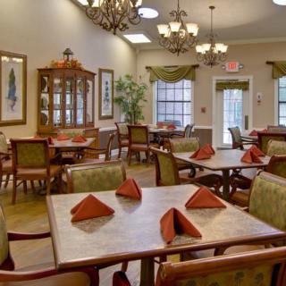 A cozy dining area with neatly arranged tables and chairs, featuring elegant chandeliers and folded napkins.