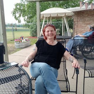 A woman enjoying a relaxing moment outdoors, seated comfortably on a chair with a pleasant background.