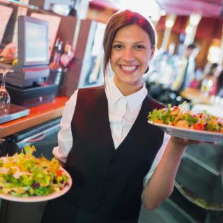 A waitress in a restaurant holding plates of food while smiling.