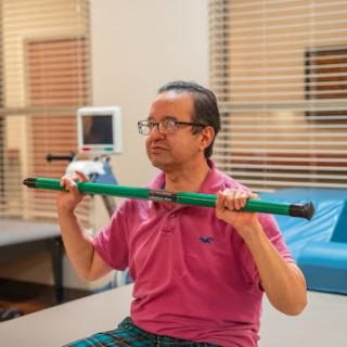 A man performs strength exercises with a green bar during physical therapy.