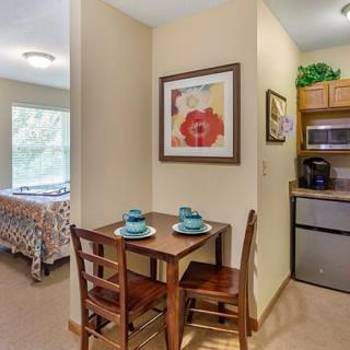 A cozy dining area with a small table set for two, adjacent to a kitchenette and a bedroom.