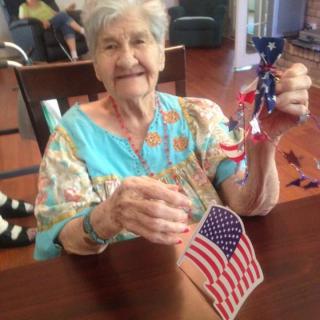 An elderly woman is smiling while holding an American flag and decorative items indoors.