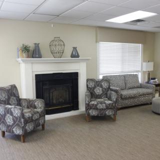 A cozy living room with a fireplace, featuring a sofa and patterned armchairs in neutral tones.