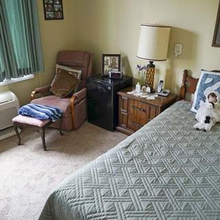 A cozy bedroom with a neatly made bed, a comfortable chair, and a side table with a lamp.