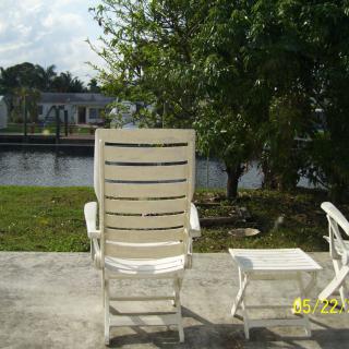 A patio chair and table set overlooking a tranquil lake with surrounding trees.