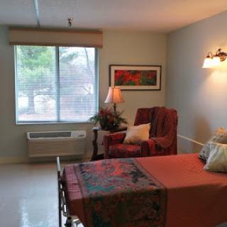 A cozy bedroom featuring a bed, an armchair, and natural light from the window.