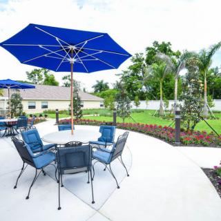 A sunny outdoor patio area with blue umbrellas and seating surrounded by a well-maintained garden.
