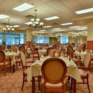 An elegant dining room with neatly arranged tables and chairs, illuminated by chandeliers.