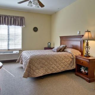 A cozy bedroom with a neatly made bed, a wooden nightstand, and a lamp, featuring a window with curtains.