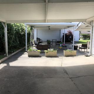 A shaded patio area under a carport with outdoor furniture and planters.