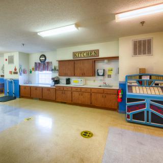 A bright and spacious daycare kitchen area with wooden cabinets and a colorful safety gate.