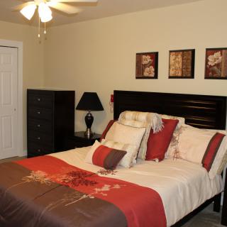 A well-decorated bedroom with a neatly made bed, vibrant pillows, and tasteful artwork on the walls.
