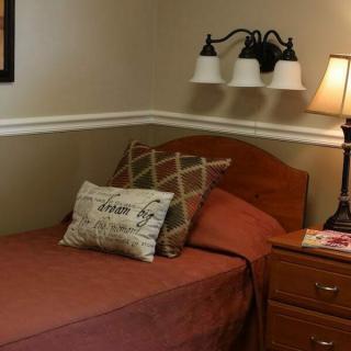 A cozy bedroom with a single bed, pillows, and a nightstand with a lamp.