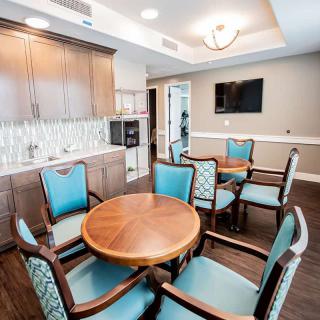 A modern seating area with a round wooden table, cushioned chairs, a wall-mounted TV, and sleek cabinetry.