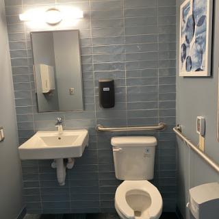 A clean and modern bathroom featuring a toilet, sink, and mirror with blue tiled walls.