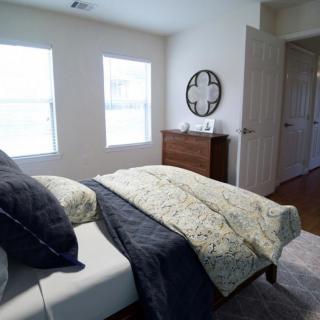A cozy bedroom featuring a bed with decorative pillows and blankets, a chest of drawers, and a wall clock.