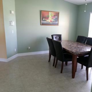 A dining room with a dark wooden table surrounded by chairs and a painting on the green wall.
