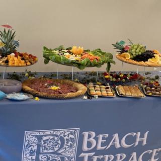 A beautifully arranged buffet table with a variety of appetizers and platters, covered by a cloth labeled 'Beach Terrace.'