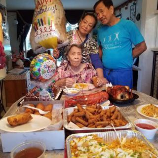 A family gathering celebrating a special occasion with a table full of diverse dishes and birthday balloons.