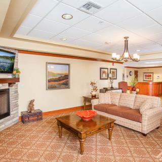 A cozy living room featuring a comfortable sofa, a wooden coffee table, and a fireplace with a mounted television. The space is decorated with artwork and illuminated by a chandelier.
