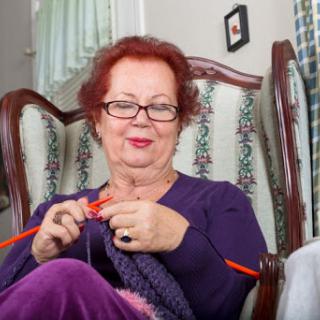 An elderly woman enjoys knitting in her cozy living room.