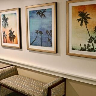 A hallway with a bench and three framed pictures of palm trees on the wall.