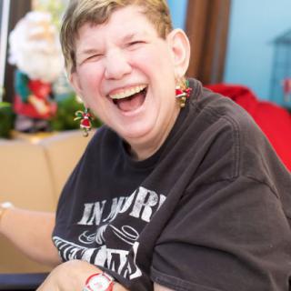 A woman smiling joyfully indoors with holiday decorations in the background.