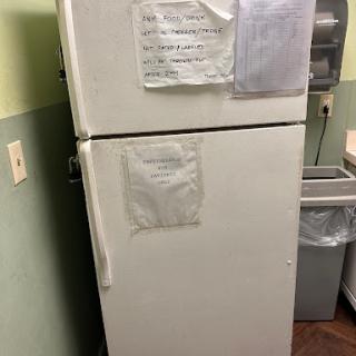A white refrigerator in a kitchen, with notes attached to its front and a trash can nearby.