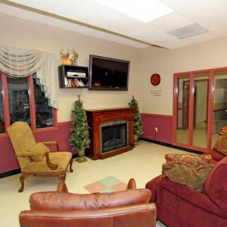 A cozy living room with a fireplace and television, furnished with comfortable chairs and decorated with plants.