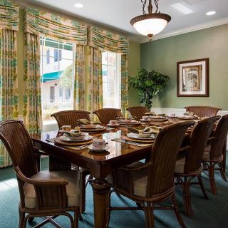 A well-decorated dining room with a large wooden table and chairs, adorned with elegant place settings and surrounded by colorful drapes.