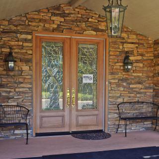 A welcoming entrance with a wooden double door surrounded by a stone wall, flanked by two benches and overhead lantern.