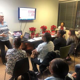A group of people attending a meeting in an office setting, with a presentation displayed on a screen.