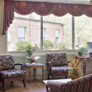 A cozy living room with patterned chairs, a side table, and large windows adorned with draped curtains.