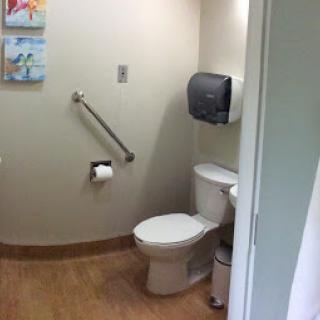 A clean and accessible bathroom featuring a toilet, handrails, and a paper towel dispenser.