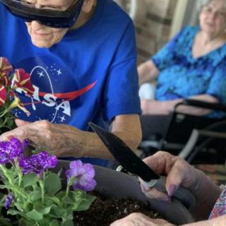 Elderly individuals engaged in gardening activities, with one wearing a NASA shirt and seated by flowers.
