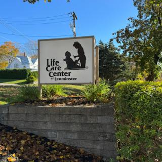 A clear blue sky frames the sign of the Life Care Center, surrounded by greenery.