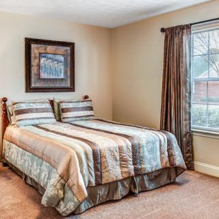 A cozy bedroom with a neatly made bed, framed artwork on the wall, and a window with curtains.