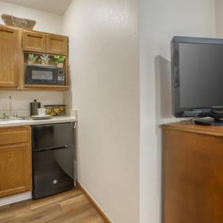 A compact kitchen area with wooden cabinets, a microwave, and a television on a separate stand.