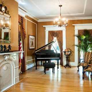 A classic living room featuring a grand piano, elegant chandelier, and timeless decor.